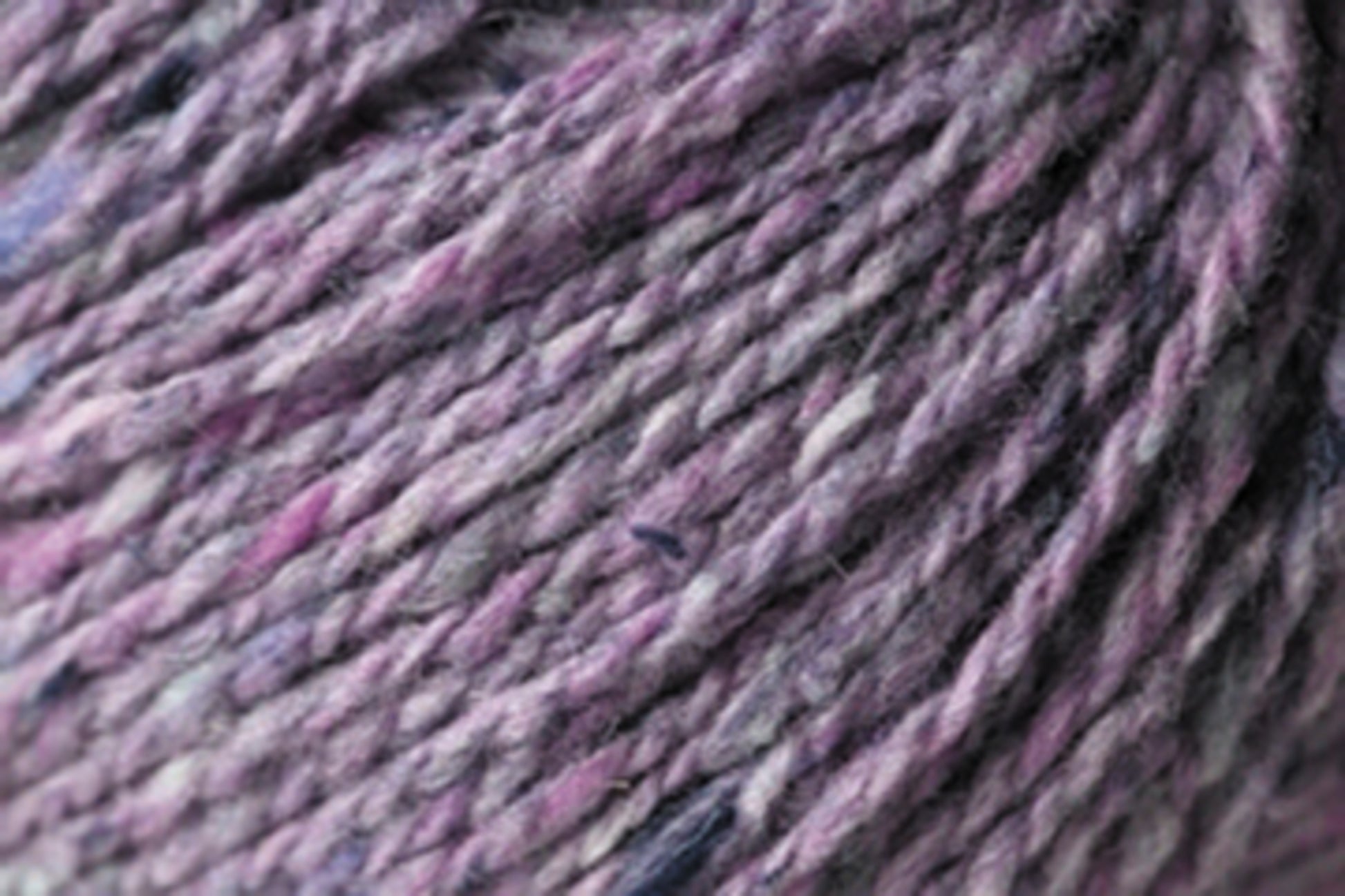 Close-up of Jo Sharp Silkroad DK Tweed by Kingfisher Yarn & Fibre in a blend of purple and grey. This DK weight yarn exhibits a slightly thick and thin texture, seamlessly mixing light and darker shades. The image captures the intricate details of the wool, silk, and cashmere fibers, highlighting the yarn's softness and density.