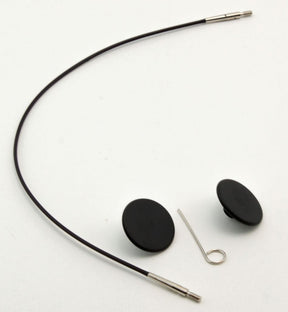 A photo of the Interchangeable Circular Needle Cord for Dreamz and Nova by Accessories Unlimited, featuring a long black cord with metal tips, two black round housings resembling interchangeable cords, and a small silver clip. The items are laid out on a plain white background.