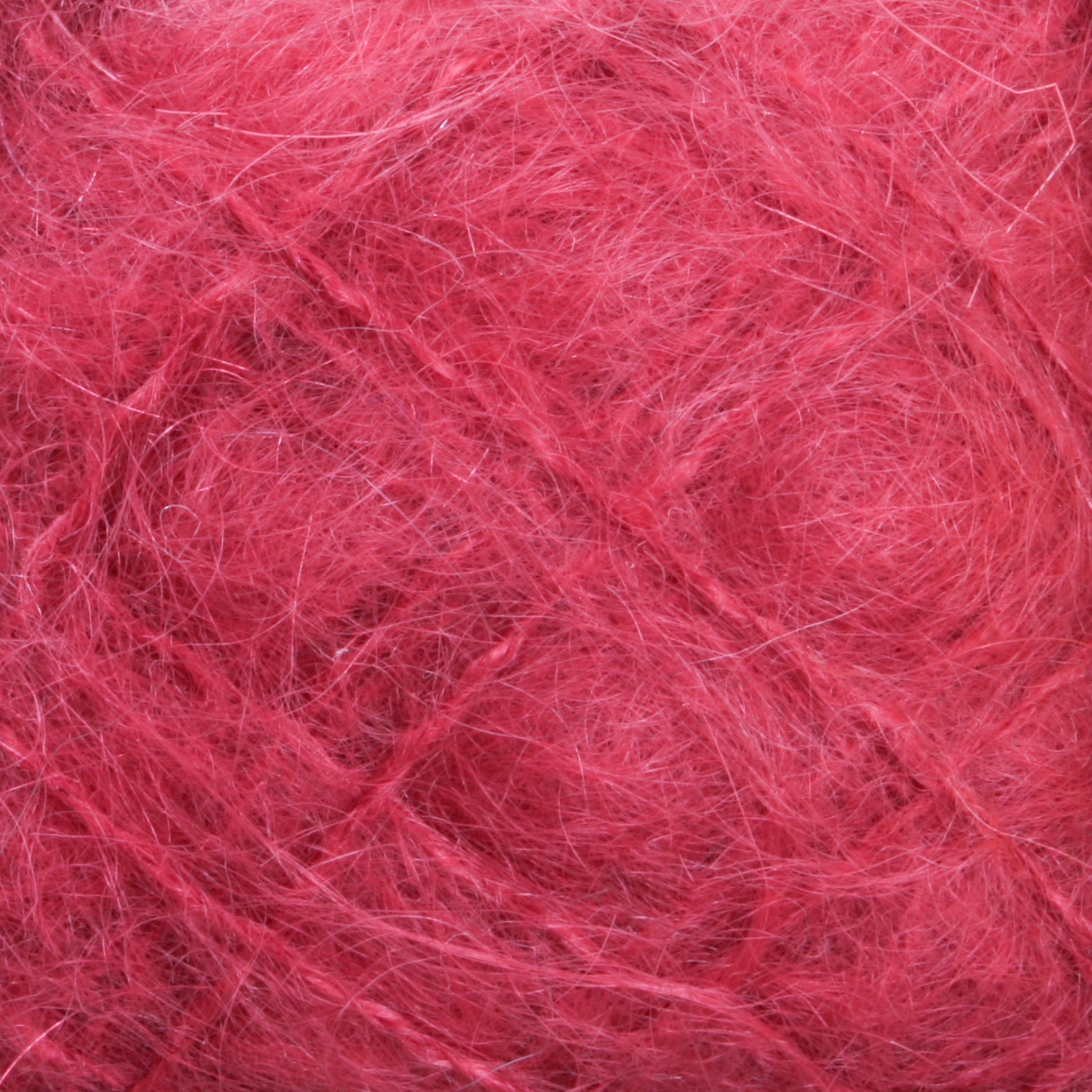 Close-up shot of a tangled mass of Victorian Brushed Mohair Yarn | Mini Skein from Caledonian Dye Works. The pinkish-red fibers display a rough and fuzzy texture, with individual strands crisscrossing and intertwining to form a chaotic yet intricate pattern. The luxurious mohair hue remains consistent throughout, with slight shading variations adding depth.