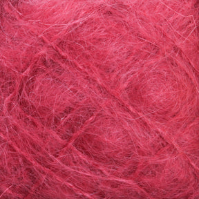 Close-up shot of a tangled mass of Victorian Brushed Mohair Yarn | Mini Skein from Caledonian Dye Works. The pinkish-red fibers display a rough and fuzzy texture, with individual strands crisscrossing and intertwining to form a chaotic yet intricate pattern. The luxurious mohair hue remains consistent throughout, with slight shading variations adding depth.