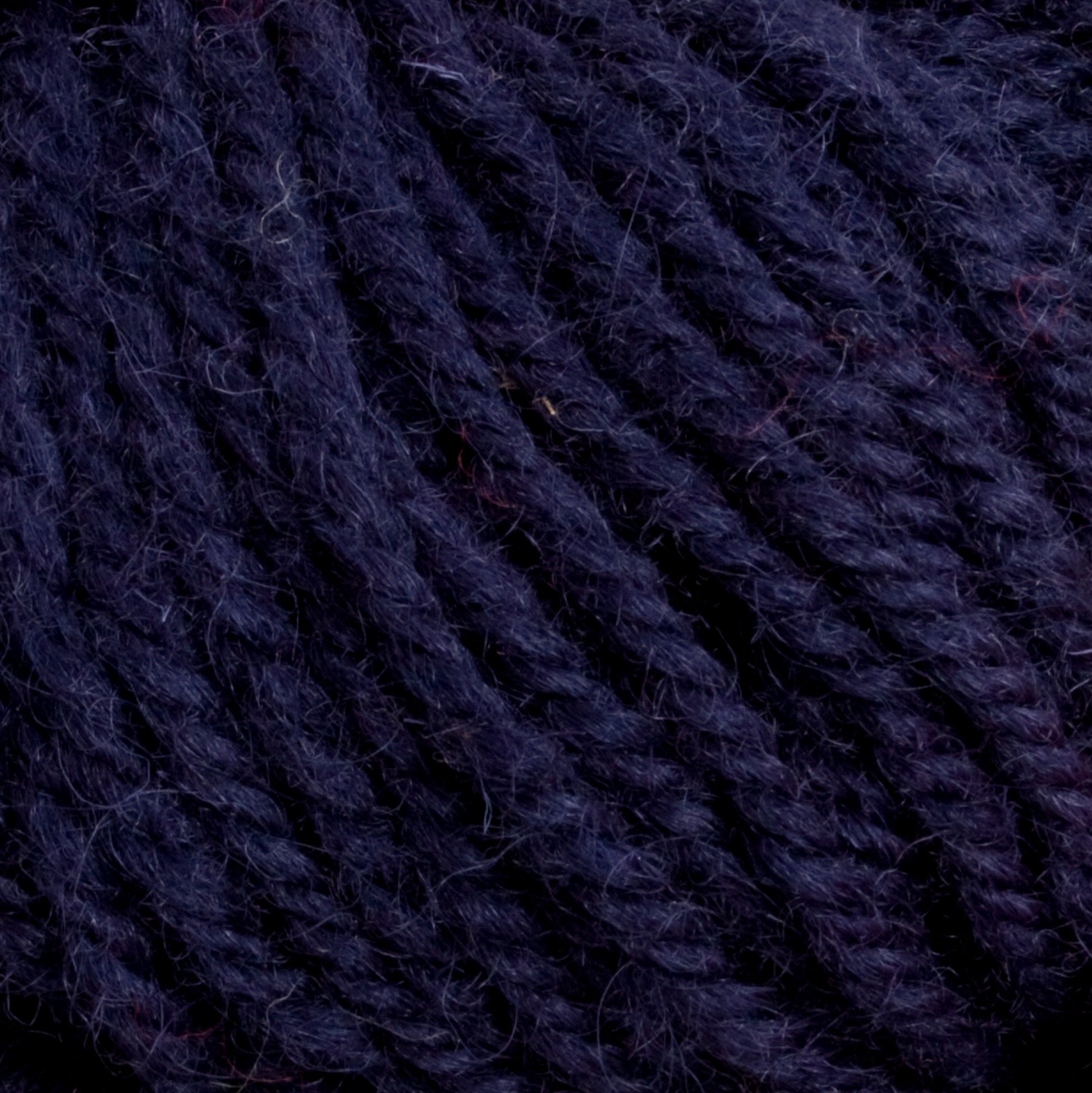 Close-up image of Caledonian Dye Works Halcyon Deco Rug Wool in a rich, dark purple hue, showcasing the tightly twisted fibers with subtle color variations and a hint of fuzziness. The 100% wool yarn has a soft and thick texture, making it perfect for knitting or crocheting projects.