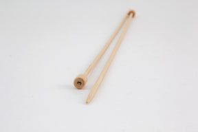 A pair of Bamboo Single-Point Knitting Needles, 12" from Accessories Unlimited lies on a white surface. One needle is placed slightly over the other in a parallel manner. The knitting needles have rounded ends with one end tapered to a point for knitting.