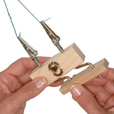 Two hands are holding the Leclerc Double Fringe Twister from Leclerc Looms, a wooden jig featuring two alligator clips attached to wires. One hand is holding the base of the twister, while the other is adjusting a part. The jig has a logo with a spiral design burned into the wood.