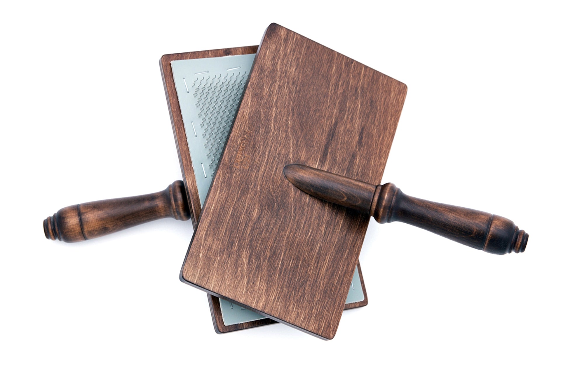 Two Kromski Hand Carders from Kromski North America, featuring wooden handles and metal teeth for carding wool or fibers, are crossed and resting against each other on a white background. The tools’ dark wood handles and rectangular wooden bases give a rustic appearance.