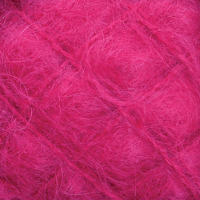 A close-up view of the Victorian Brushed Mohair Yarn from Caledonian Dye Works reveals its fuzzy, bright pink fibers, creating a soft and textured appearance. The intertwining strands give this large skein of yarn a slightly tangled, fluffy look reminiscent of luxurious mohair.