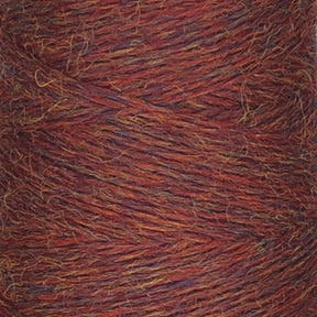 A close-up view of a spool of JaggerSpun Heather 3/8 yarn by Jagger Brothers, Inc. reveals a gradient featuring vibrant hues of red, orange, and subtle hints of purple and blue. The worsted spun wool fibers are tightly wound in a diagonal pattern, showcasing the intricate texture and the multicolored strands interwoven together.