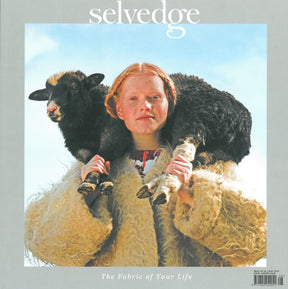 A person with red hair wearing a shaggy, oversized coat carries a black sheep on their shoulders against a soft blue sky backdrop. At the top of the image is the text "Selvedge," and at the bottom, it reads "Selvedge - Issue 108: Farm; From Field to Fabric," symbolizing our connection to fibre farmers and organic products.