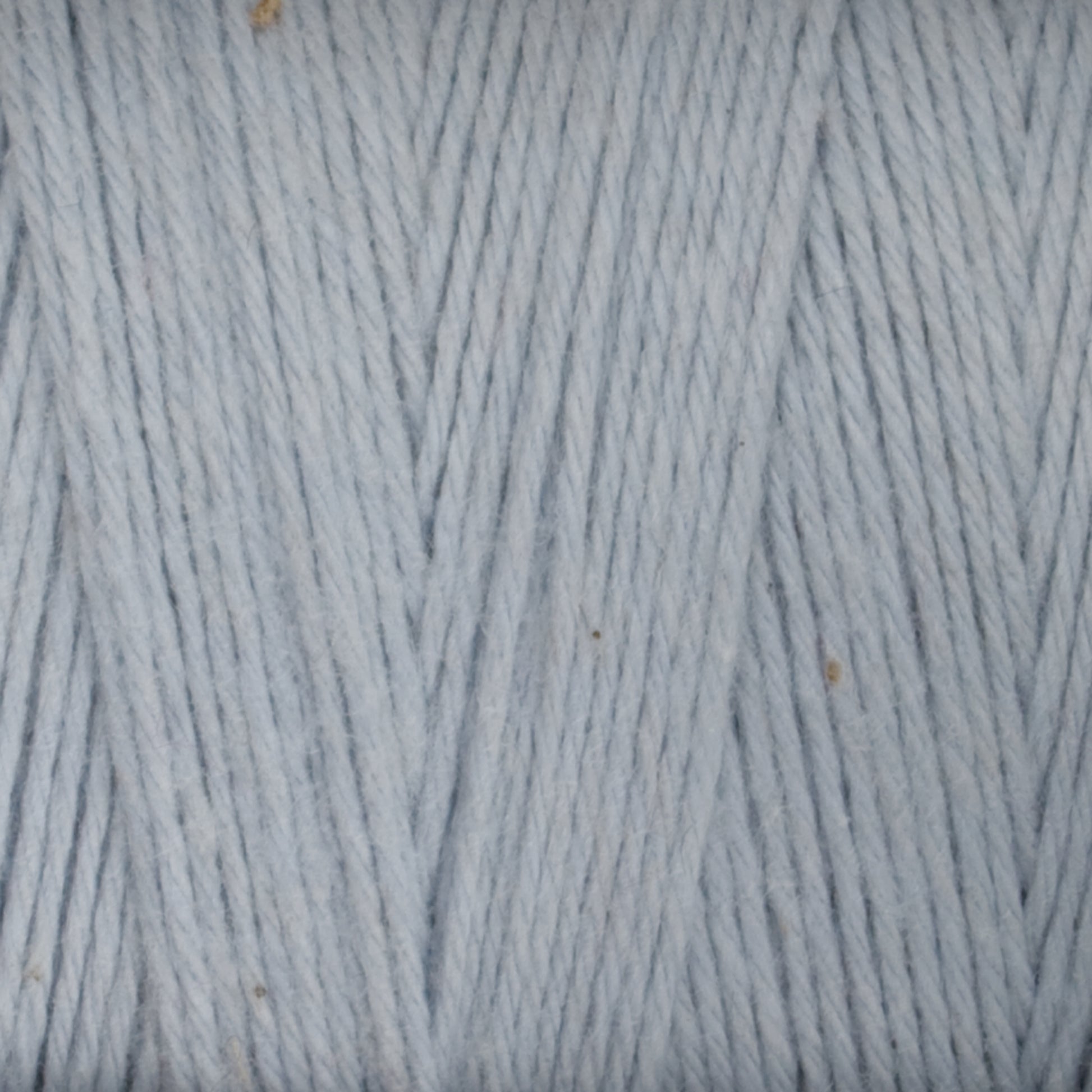 A close-up image of **Maurice Brassard's Medium Cotton 16/8 Mop Yarn**, tightly wound and showcasing a smooth, even texture. The yarn strands, made from sturdy cotton, run vertically with some interwoven diagonally, highlighting the fine quality perfect for weaving. Small specks are visible, adding subtle detail.