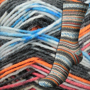 A single, multicolored knit sock with intricate Fair Isle patterns, showcasing shades of orange, blue, white, and brown from the Regia 4-ply Design Line by Arne & Carlos collection by Sirdar - Regia, Schachenmayr & Rowan, is displayed in front of a background of thick, multicolored self-pattern sock yarn strands in the same hues.