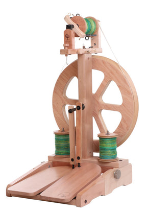 The Ashford Kiwi 3 Spinning Wheel by Ashford Handicrafts Limited is a modern spinning wheel with a wooden base, hand crank, and large wheel for spinning yarn. It features two spools of green and blue thread, a built-in stand, folding treadles, and a foot pedal for operating the spinning mechanism.