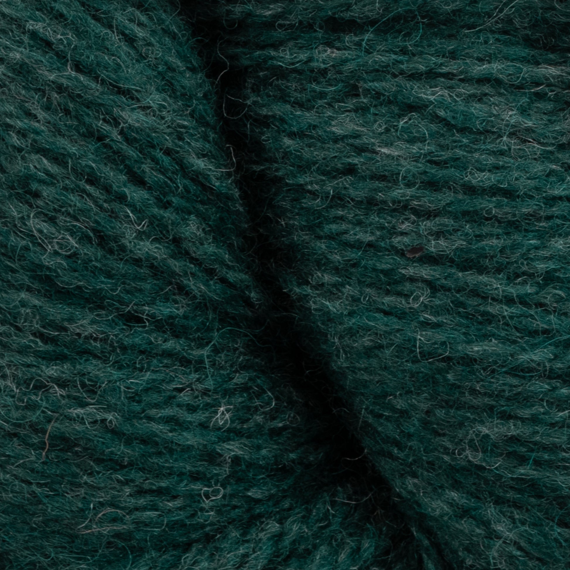 Close-up image of a dark green, textured wool yarn. The fibers, made from GOTS certified Patagonia Organic Merino by Juniper Moon Farm, are intertwined and slightly fuzzy, showcasing the natural texture and softness of the Knitting Fever / Euro Yarns creation.