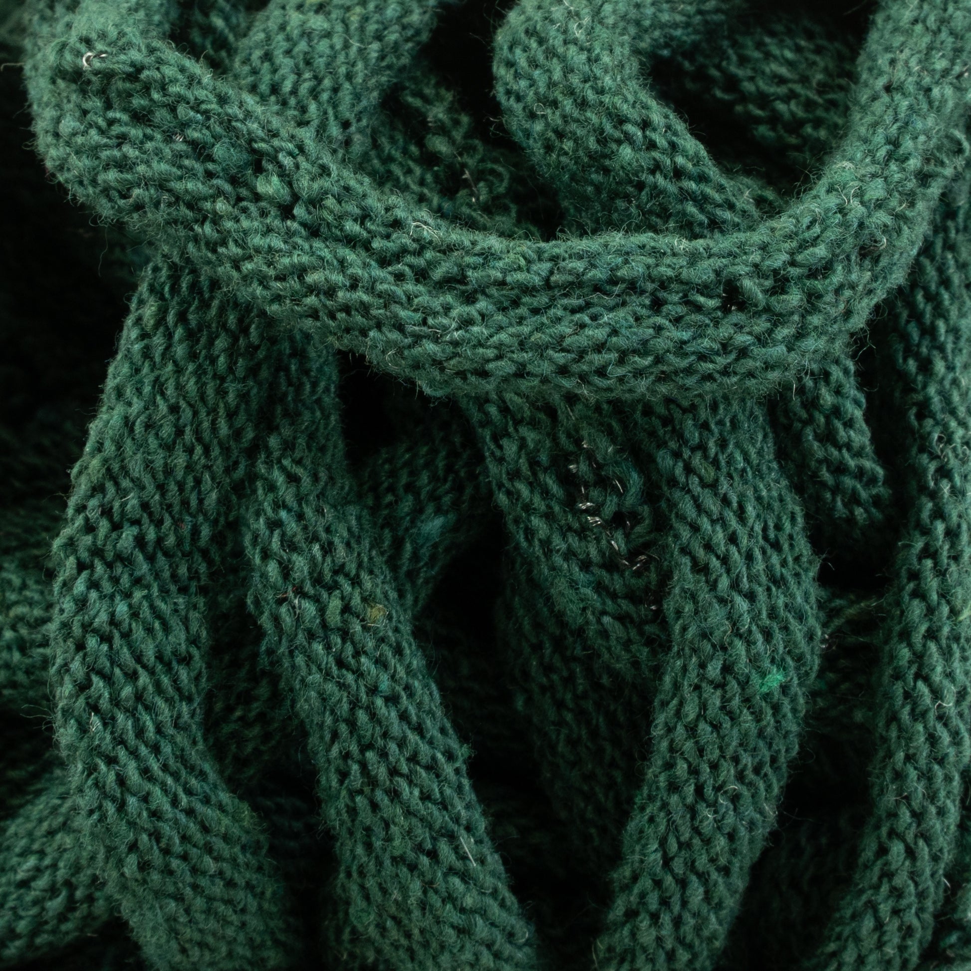 Close-up of the Harrisville Potholder Loops - Traditional Size Mini Pack by Friendly Loom, featuring a textured, dark green knitted fabric with loose, intertwined cotton loops. The yarn fibers are clearly visible, showcasing a detailed and intricate weave pattern. The image emphasizes the texture and structure of the knitting as crafted on a potholder loom.