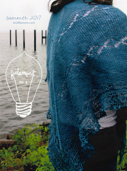 A person stands near a body of water wearing a teal knitted shawl over their shoulders. The backdrop features wooden posts emerging from the water. Text reads "Knit Filament" with a light bulb graphic labeled "Filament No. 3 Summer 2017." This scene epitomizes modern classics in our full-color magazine on knitwear patterns.