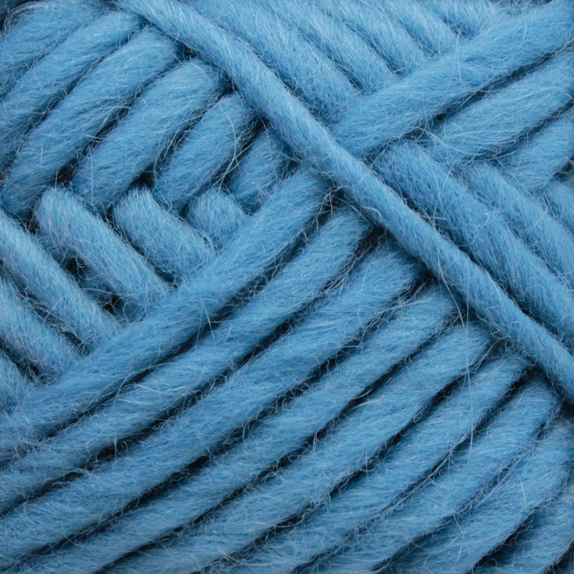 A close-up image of Brown Sheep's Lamb's Pride Bulky Yarn in light blue. The thick, soft strands are tightly wound together, showcasing their fluffy texture and fibrous details. Perfect for knitters and crocheters, the yarn appears ready for crafting cozy woven blankets or Icelandic sweaters.