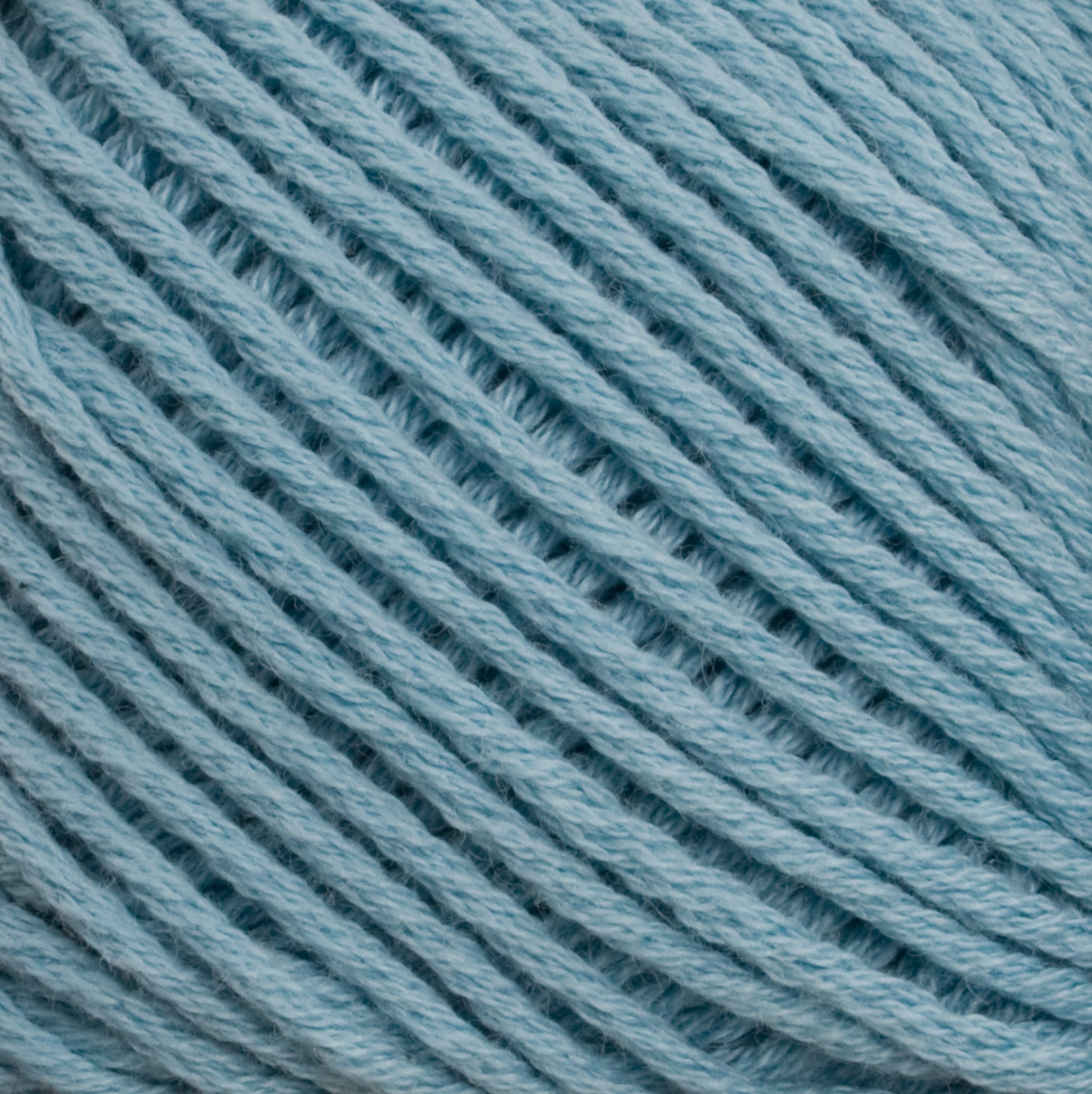 Close-up image of Brown Sheep's Cotton Fleece yarn in light blue, expertly wound into a tight, orderly coil. The fibrous texture and intertwined strands are clearly visible, highlighting the softness and uniformity of the yarn—ideal for creating intricate knitting patterns.