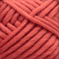 Close-up image of thick, soft Lamb's Pride Bulky Yarn in a warm coral color. The strands are wound together, creating a textured pattern of overlapping fibers. The yarn, by Brown Sheep, appears plush and cozy, perfect for knitters and crocheters crafting Icelandic sweaters or woven blankets.