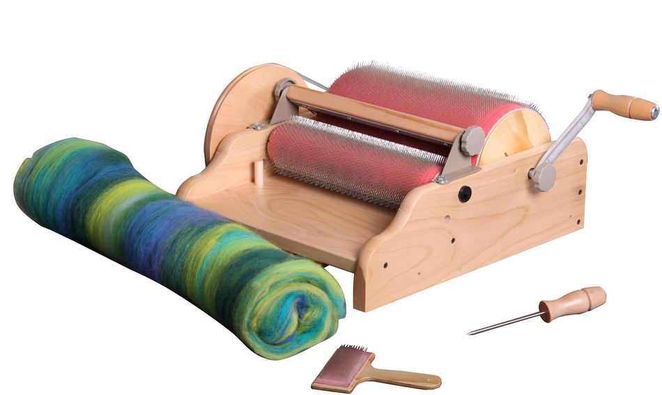 An Ashford Drum Carder - Fine 72 pts by Ashford Handicrafts Limited, designed with metal teeth, is displayed next to a vibrant roll of wool in shades of green, blue, and yellow. Accompanying the display are a small brush and a wooden-handled tool.