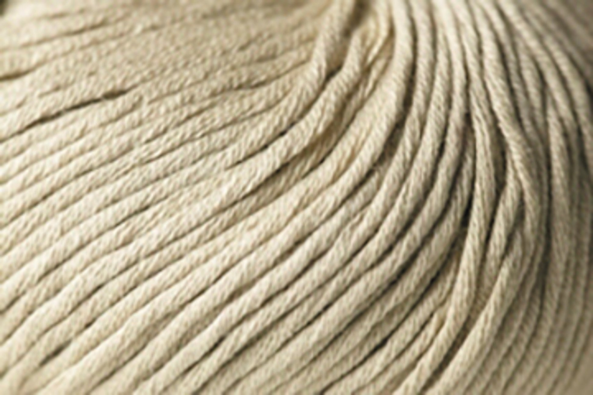 Close-up image of a beige Jo Sharp Soho Summer DK Cotton yarn ball from Kingfisher Yarn & Fibre, displaying the tightly wound strands of fiber. The texture appears soft and smooth, with the strands neatly arranged in parallel lines. The image captures the intricate details of this summer yarn’s composition.