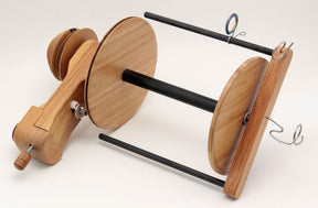 The Majacraft Aura Overdrive Head, made by Majacraft Co., features a wooden spinning wheel bobbin and flyer assembly with two large wooden discs attached to a central axis. The apparatus includes several metal hooks and brackets, specifically designed for hand spinning yarn on a Majacraft spinning wheel. Its large volume bobbins are perfect for extensive projects and are presented on a light surface.