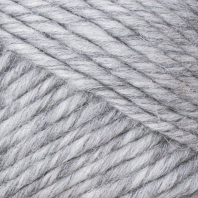 Close-up view of Lamb's Pride Bulky Yarn by Brown Sheep in light gray, highlighting its soft, textured fibers twisted together in a diagonal pattern. The yarn appears thick and slightly fuzzy, making it perfect for knitters and crocheters crafting cozy woven blankets.