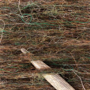 A close-up view showcases the soft, multicolored hues of Plötulopi Unspun Icelandic Wool Yarn by Berroco, Inc., featuring shades of green, brown, and tan that create a richly textured and intertwined pattern. A wooden knitting needle is partially visible, embedded in the yarn, indicating a knitting project in progress.