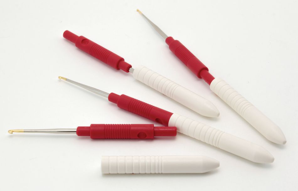 Five Capped Steel Crochet Hooks from Skacel, featuring a sleek white plastic design with red accents and slender metal tips. These tools are laid out on a flat surface, with some showing retracted tips while others are extended. Boasting comfortable handles and protective caps, they resemble steel crochet hooks used in electronics or small-scale mechanical work.