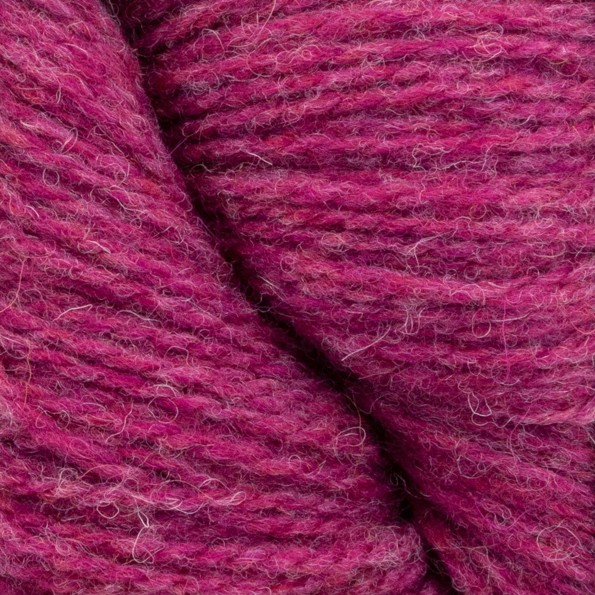 Close-up view of two skeins of Patagonia Organic Merino by Juniper Moon Farm, showcasing shades varying from light pink to deep red. The texture of this luxurious yarn by Knitting Fever / Euro Yarns is soft and slightly fuzzy, with visible fibers enhancing its plush appearance. It is GOTS certified, ensuring quality and sustainability.