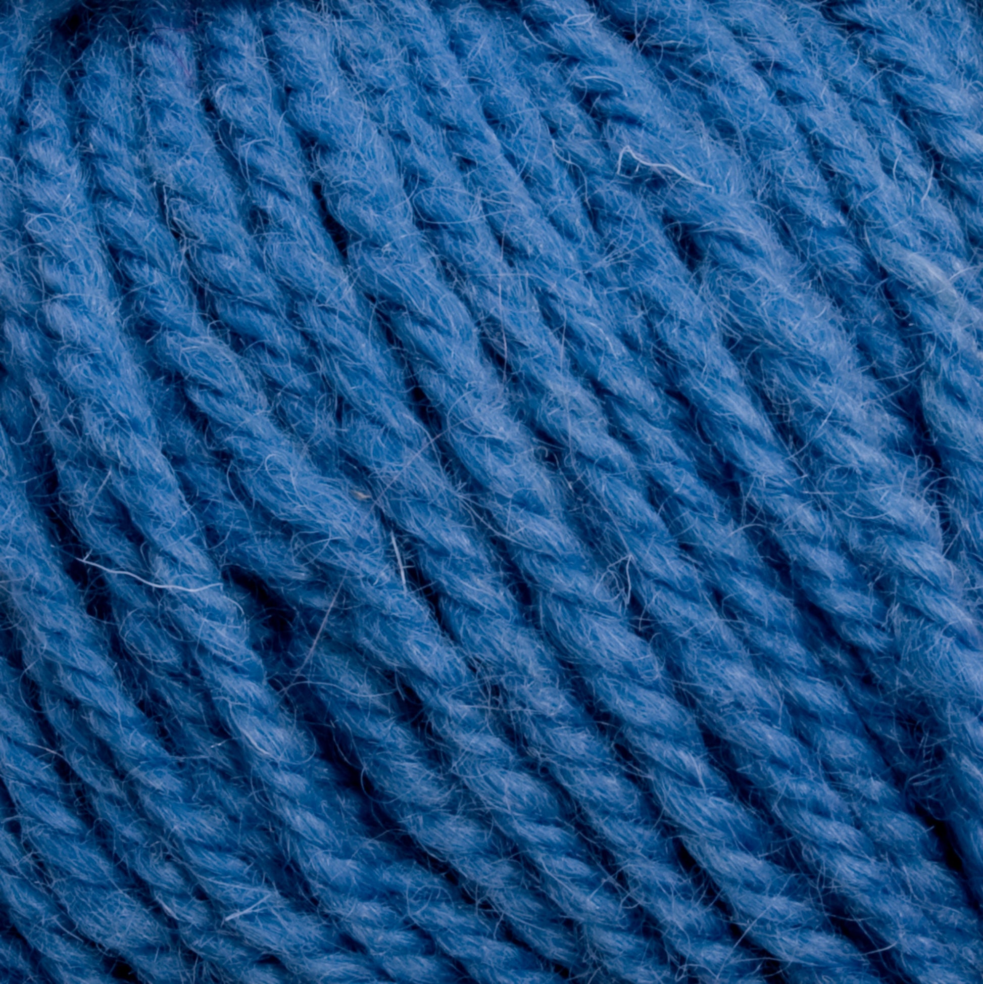 Close-up view of thick, textured Halcyon Deco Rug Wool from Caledonian Dye Works, tightly wound into a ball. The 100% wool yarn has a slightly fuzzy surface, showing individual fibers and a rich, vibrant blue hue, ideal for versatile knitting or crocheting projects.