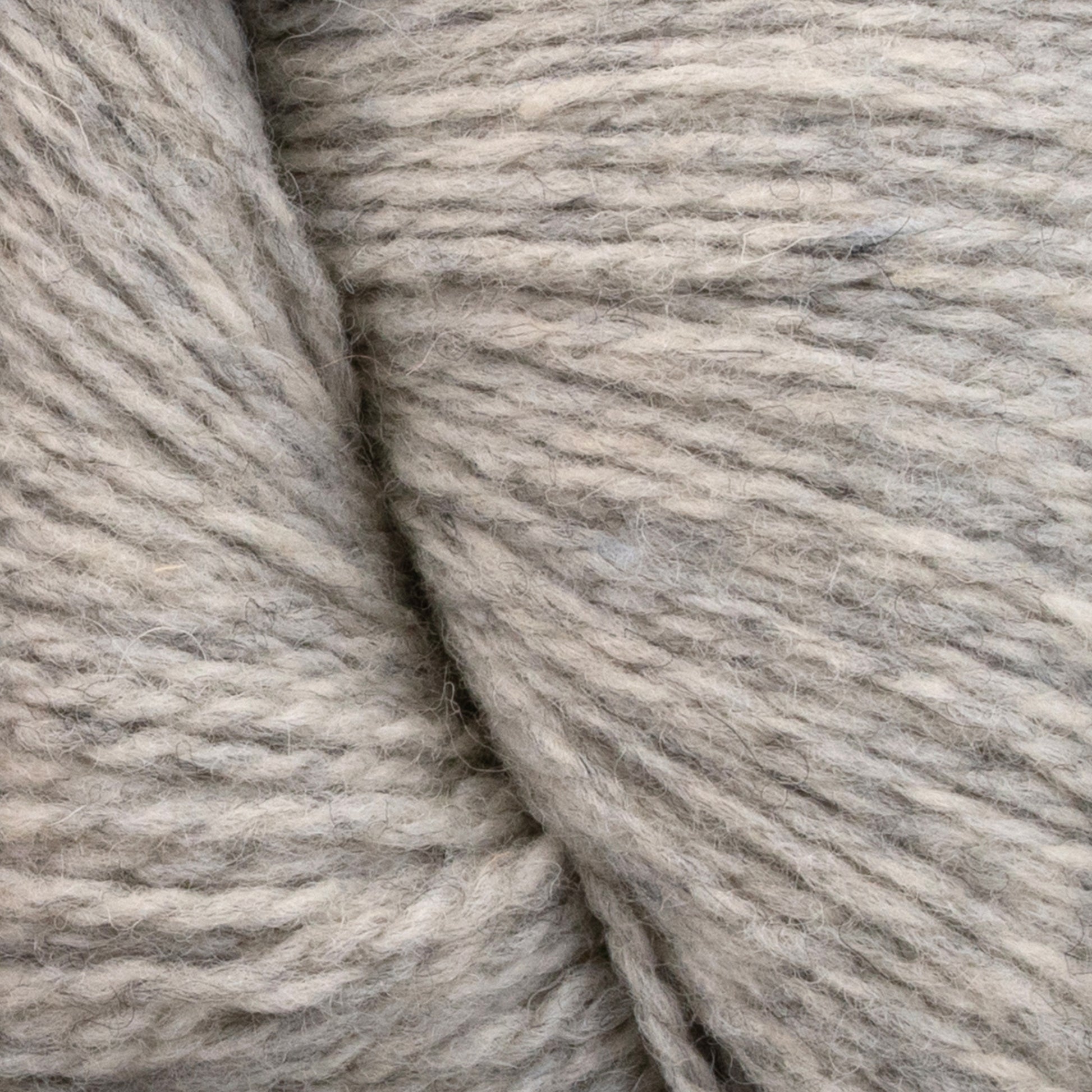 Close-up of a hank of natural, undyed beige yarn made from Patagonia Organic Merino by Juniper Moon Farm. The fibers are loosely twisted, showcasing the texture and subtle variations in color. The image highlights the softness and warmth of this GOTS certified material from Knitting Fever / Euro Yarns.