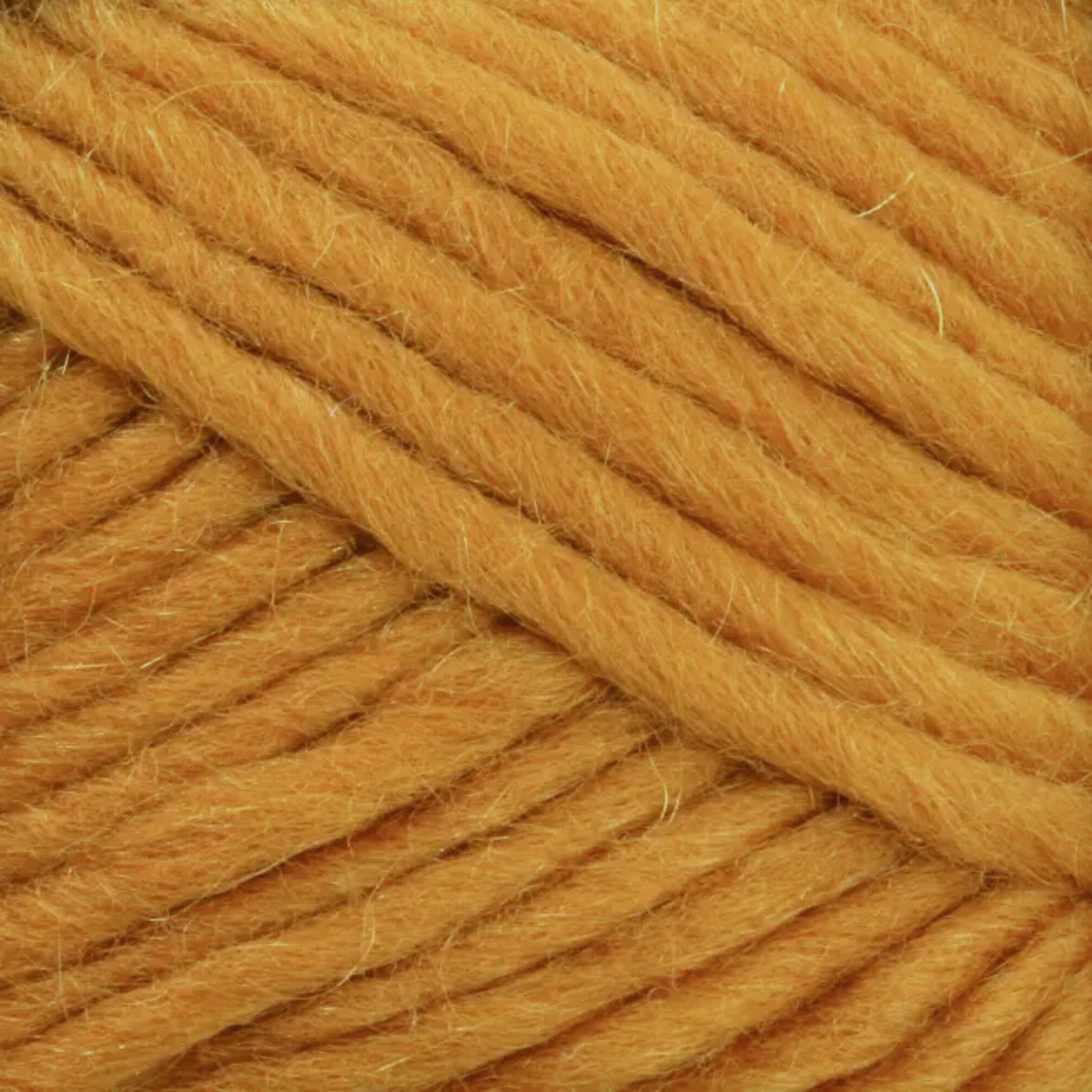 Close-up of a ball of Lamb's Pride Bulky Yarn, showcasing its thick golden-yellow strands and soft texture. The yarn, by Brown Sheep, appears to be loosely spun, making it an ideal choice for knitters and crocheters who desire a fluffy, slightly fuzzy surface for crafting cozy Icelandic sweaters.