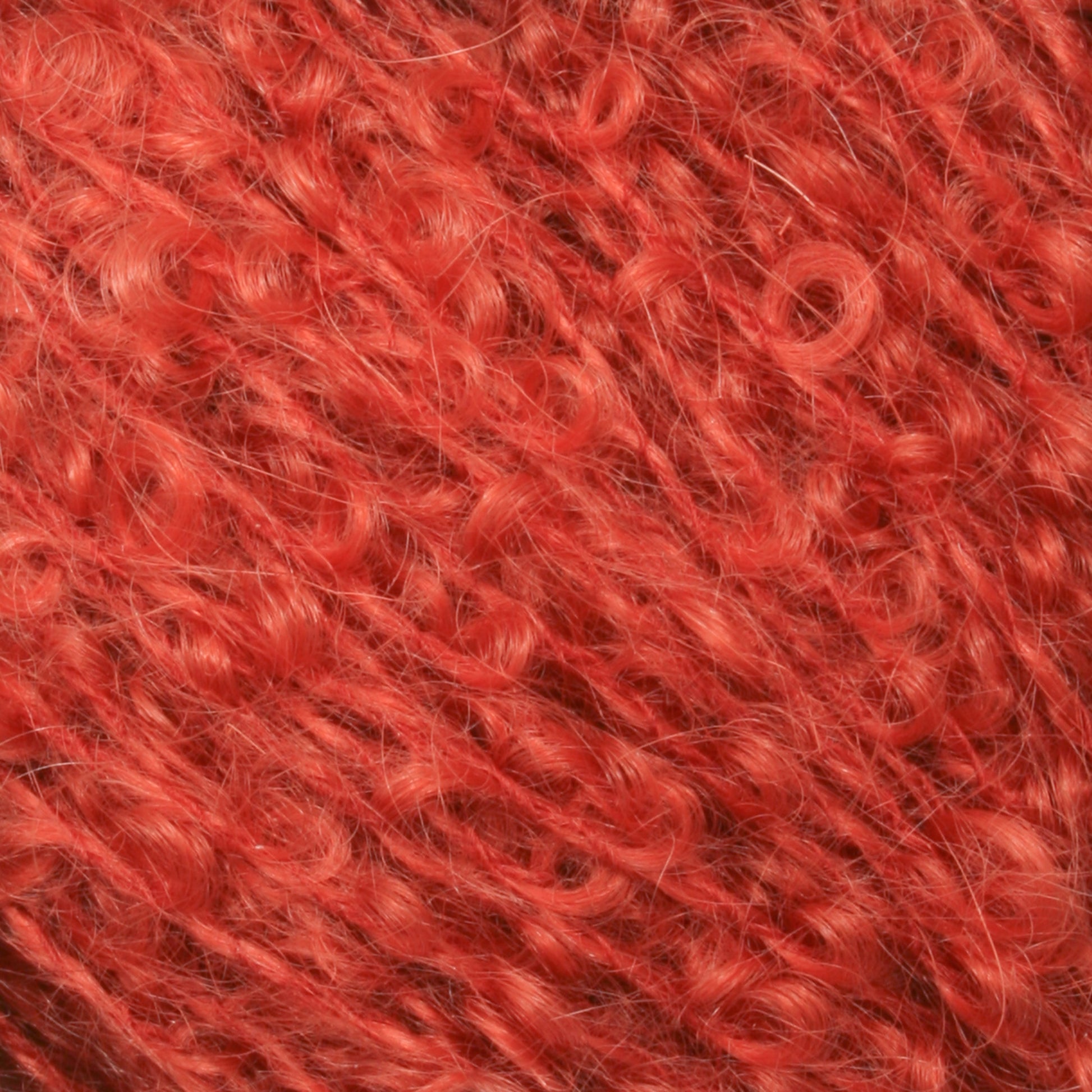 Close-up of a bundle of fuzzy, curly, red yarn fibers from Caledonian Dye Works. The Victorian Bouclé Mohair Yarn has a thick, textured appearance with intertwined strands creating a tangled yet soft look. The vibrant color and mohair bouclé texture make it a standout from Halcyon's Signature Victorian Collection.