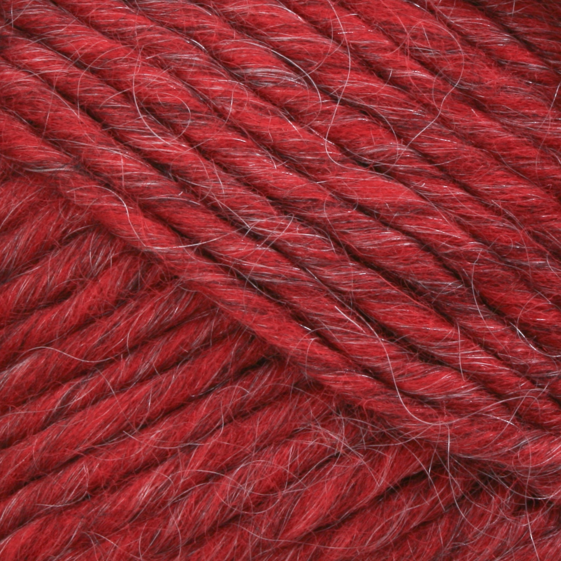 A close-up image showcases the vibrant red Lamb's Pride Bulky Yarn from Brown Sheep, featuring a soft, slightly fuzzy texture. The yarn strands are tightly twisted together, creating a thick and robust appearance. Interspersed thin, lighter-colored fibers add depth to the overall hue—ideal for knitters and crocheters creating Icelandic sweaters.