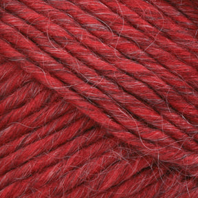 A close-up image showcases the vibrant red Lamb's Pride Bulky Yarn from Brown Sheep, featuring a soft, slightly fuzzy texture. The yarn strands are tightly twisted together, creating a thick and robust appearance. Interspersed thin, lighter-colored fibers add depth to the overall hue—ideal for knitters and crocheters creating Icelandic sweaters.