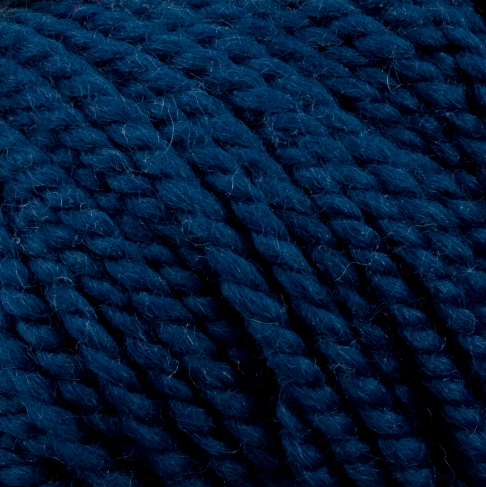 Close-up image of thick, dark blue yarn, showing its twisted strands and soft texture. Made from 100% U.S. wool, the Norumbega Aran weight yarn by Caledonian Dye Works features tightly wound fibers that create a plush and dense appearance.