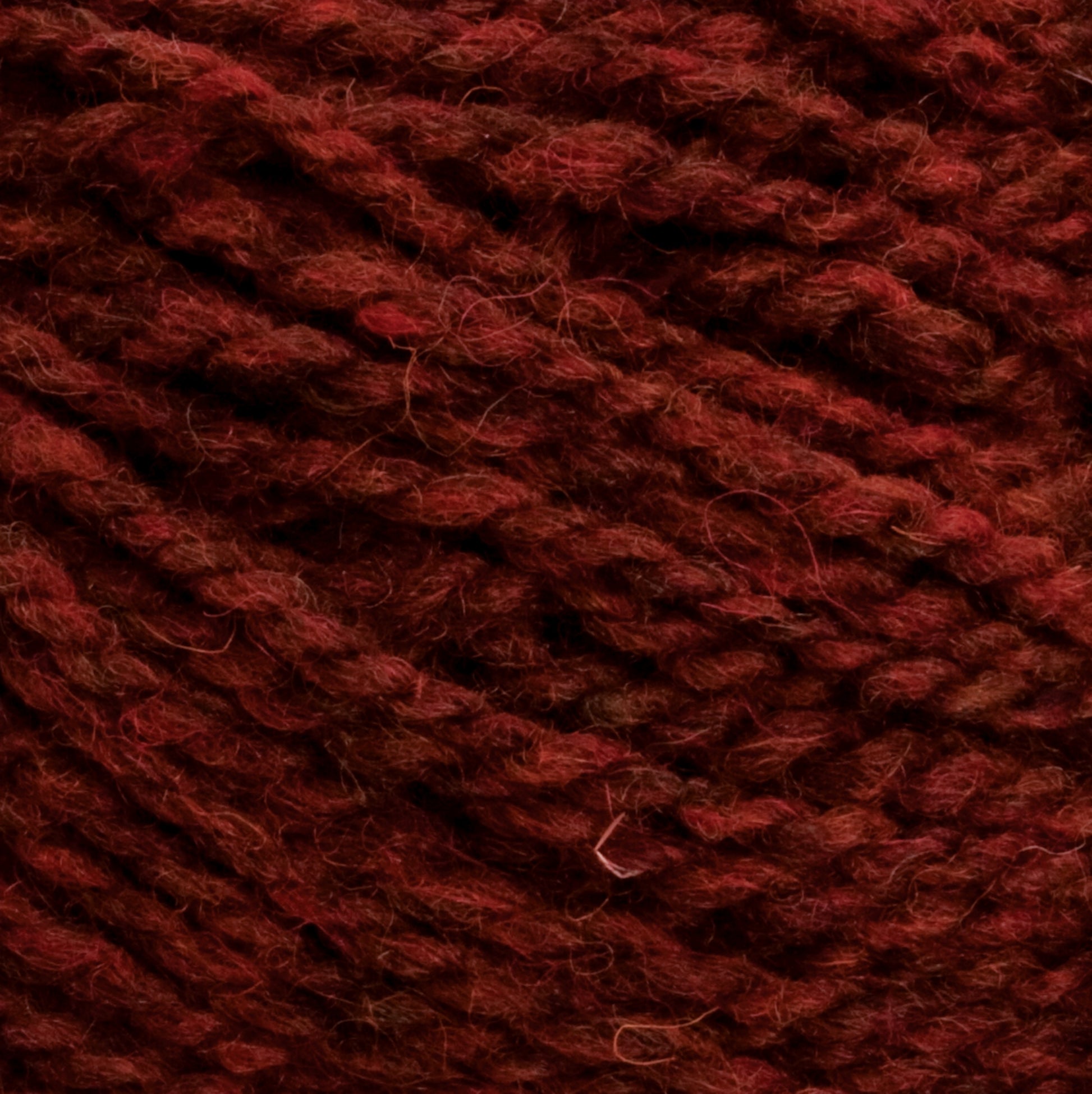 Close-up view of deep red wool yarn, tightly wound in a coil pattern. The Harrisville Designs Shetland Yarn - Unwashed Cones texture appears soft and slightly fuzzy, with visible fibers and a rich, warm color—perfect for crafting lightweight blankets or Fair Isle knitting designs.