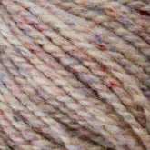 Close-up image of beige Bartlettyarns' Bartletts Maine Wool - Sport yarn, featuring multicolored flecks in shades of pink, blue, and purple. The texture appears soft and slightly fuzzy with tightly twisted strands. The colors are subtly blended, creating a speckled effect throughout this sport weight yarn.