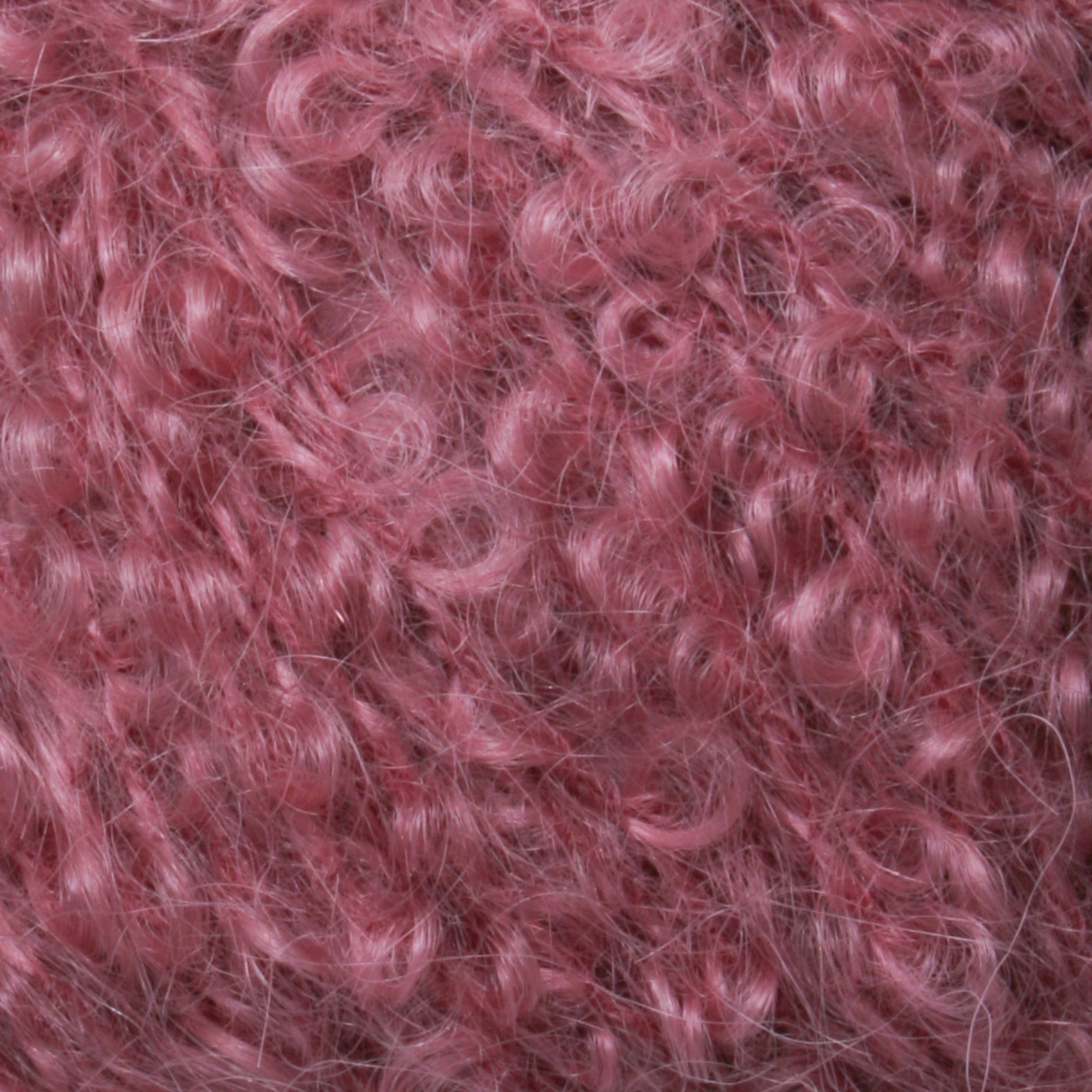 Close-up image of a mass of curly, pink synthetic fibers, resembling soft, fluffy yarn or hair. The texture is dense, with individual curls and strands visible, creating a rich and intricate pattern—a distinctive piece from Caledonian Dye Works' Victorian Bouclé Mohair Yarn Collection.