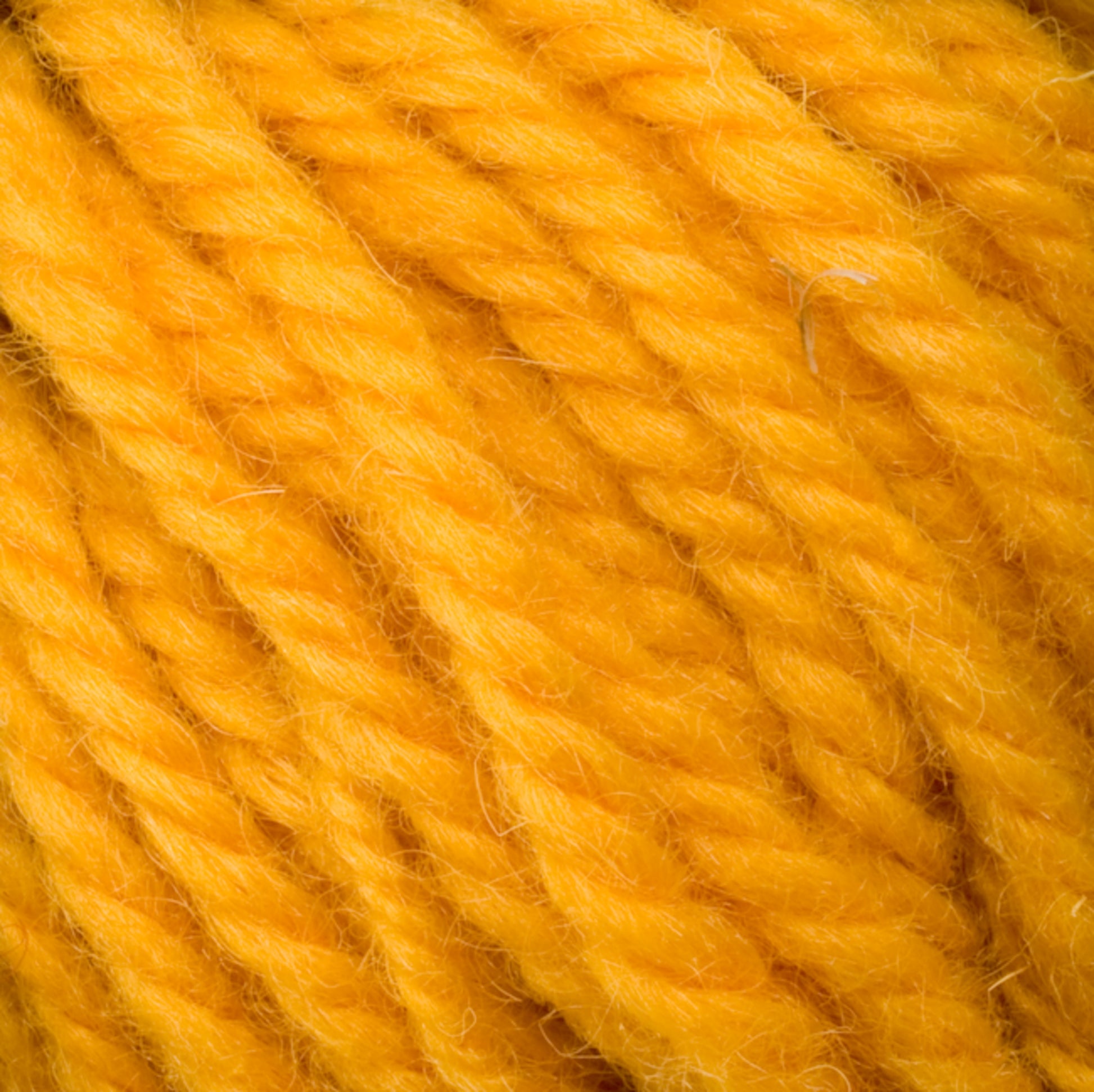 Close-up view of Halcyon Yarn Classic Rug Wool by Caledonian Dye Works in a vibrant yellow color, twisted into strands. The fibers are slightly fuzzy, creating a soft texture. The individual strands are tightly wound together, showcasing the bright hue and intricate details of this quintessential rug wool preferred by weavers.