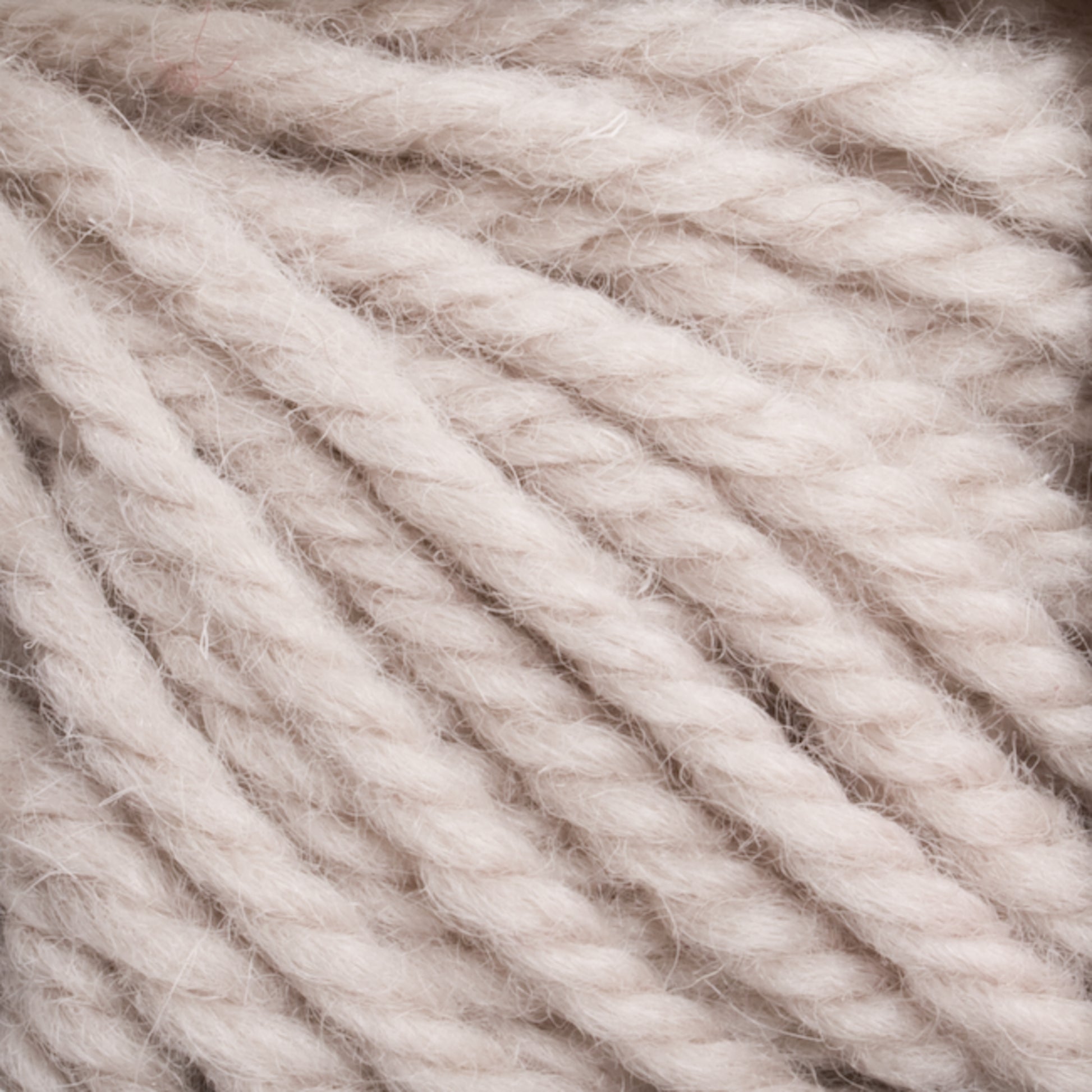 Close-up of thick, soft, cream-colored Halcyon Yarn Classic Rug Wool, showcasing the detailed texture and twist of the fibers by Caledonian Dye Works. The yarn appears fluffy and slightly fuzzy, highlighting its cozy and plush characteristics. Ideal for knitting or crocheting warm garments, this hand-dyed creation is also perfect for weavers using rug wool.