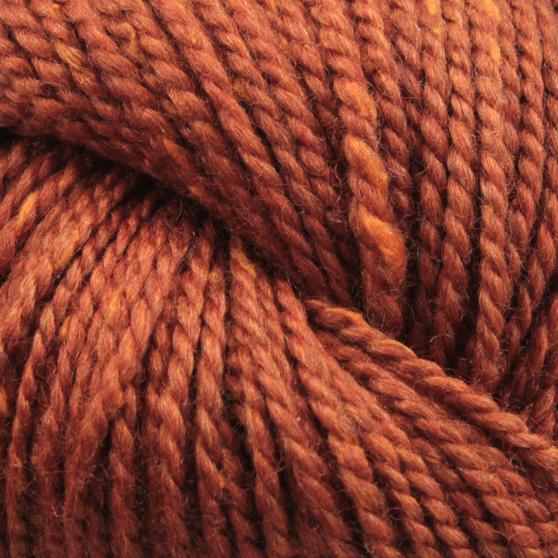 Close-up image of thick, twisted strands of Acadia by The Fiber Company yarn from The Fibre Co. (UK) Ltd, showing its texture and fibers in fine detail with a subtle tweed effect. The reddish-brown yarn appears soft and is tightly wound, suggesting it is ready to be used for knitting or crocheting.