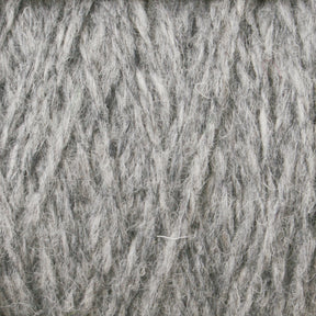 A close-up image of a tightly coiled bundle of Harrisville Shetland Yarn - Unwashed Cones from Harrisville Designs, showing detailed textures and fibers. The yarn appears thick and soft, with slightly varying shades of gray—ideal for Fair Isle knitting designs or crafting lightweight blankets.