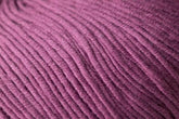 Close-up image of Jo Sharp Soho Summer DK Cotton from Kingfisher Yarn & Fibre. The purple fabric features a ribbed pattern and tightly woven threads, creating a uniform surface across the lightweight cotton material. The color appears consistent, with subtle variations due to lighting.