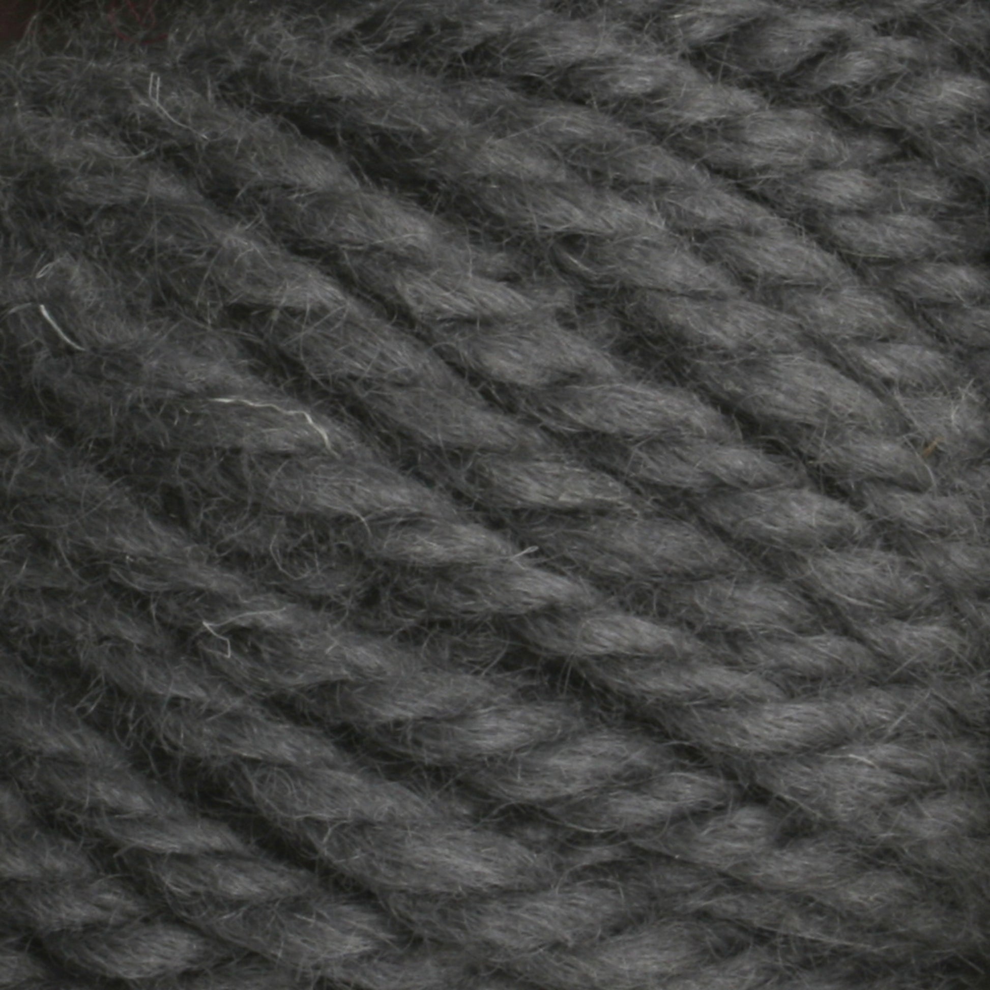 Close-up image of Halcyon Yarn Classic Rug Wool | Skein by Caledonian Dye Works. The thick, dark gray yarn features a slightly fuzzy texture and is tightly twisted in plies. The fibers appear soft and well-defined, making it ideal for knitting or crocheting projects. Perfect for weavers looking to incorporate this high-quality rug wool into their hand-dye creations.