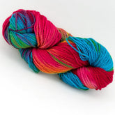 A skein of the Great Adirondack Organic DK Cotton yarn by Great Adirondack Yarn Co, Inc. showcases vivid, variegated colors in shades of red, blue, green, and yellow, neatly coiled against a white background. This hand-dyed creation offers the natural luxury of organic cotton yarn.