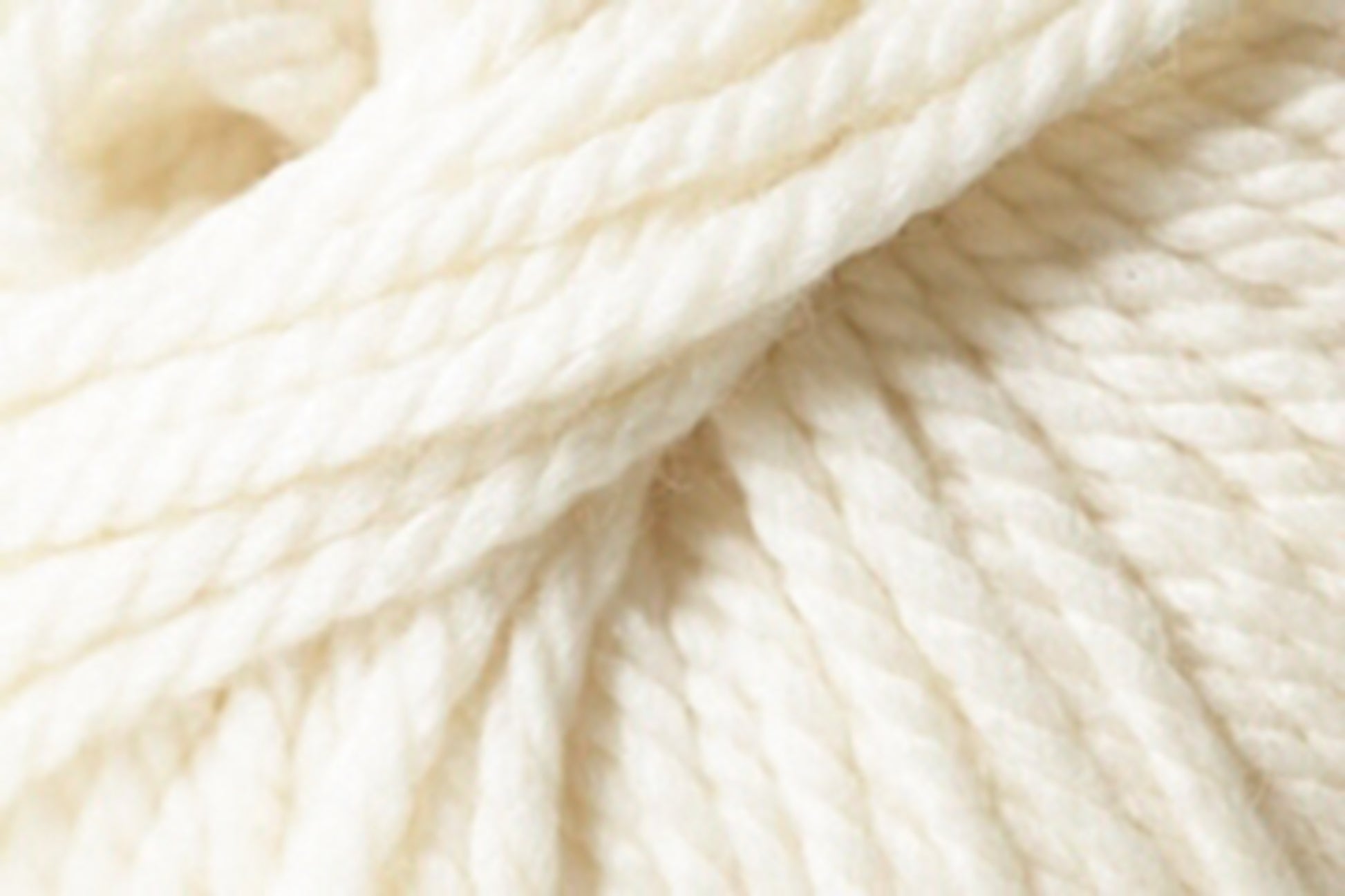 A close-up of Jo Sharp Silkroad Ultra, a thick, loosely twined cream-colored yarn from Kingfisher Yarn & Fibre. The texture appears super soft and slightly fluffy, suggesting it is crafted from high-quality natural fibers. Ideal for cozy winter accessories, the strands twist together to form a continuous, durable material.