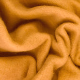 Close-up of a piece of soft, wrinkled Merino Prefelt by Europa Wools Ltd in a warm, golden-brown color. The fabric has a fuzzy texture and the folds create an abstract pattern, perfect for nuno felting projects.