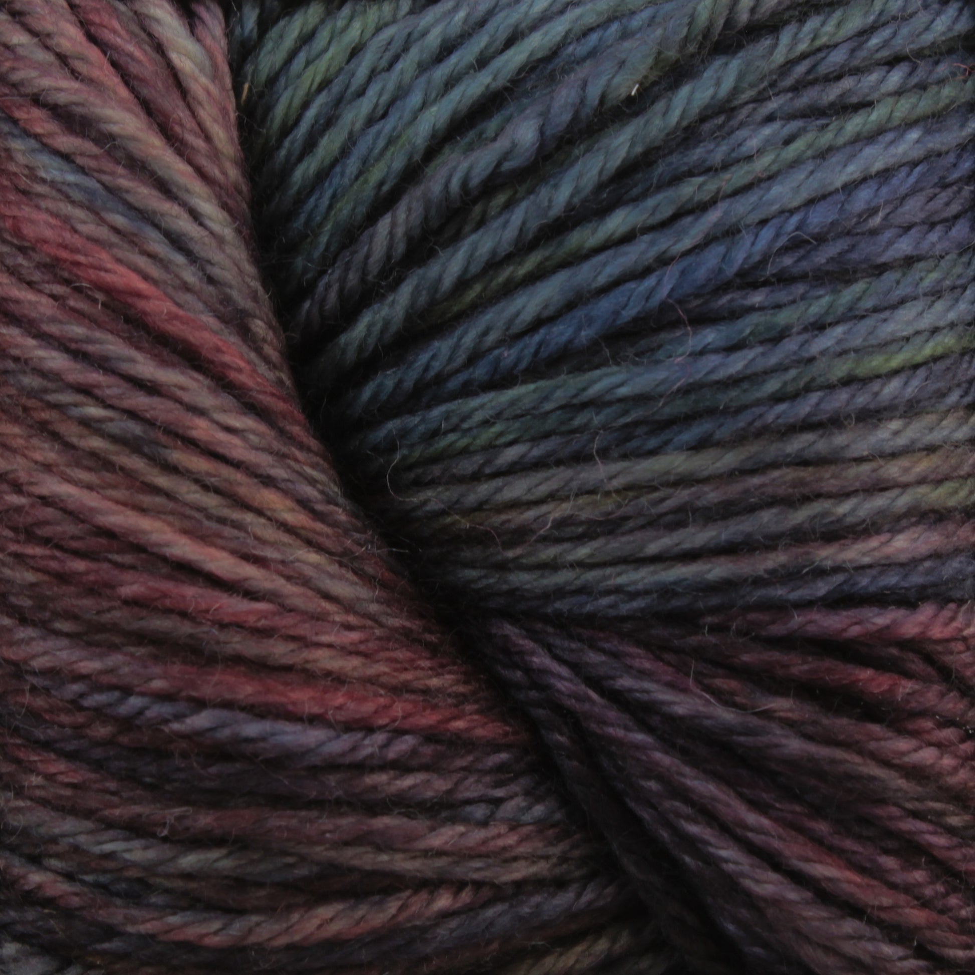 Close-up image of Malabrigo Yarn's Malabrigo Arroyo, highlighting the deep, rich shades of red, blue, green, and purple that blend together seamlessly. This sport weight superwash merino wool yarn appears soft and thick, making it perfect for knitting or crocheting lightweight garments.