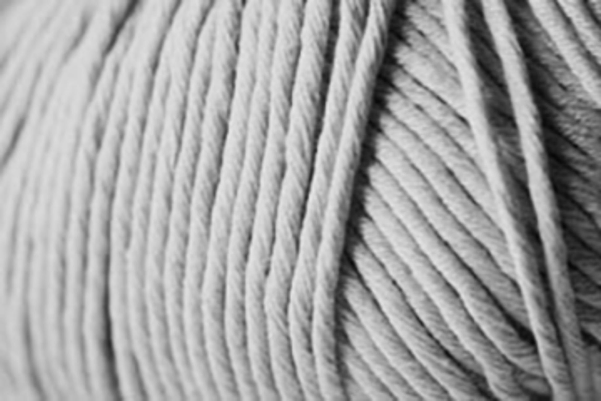 Close-up image of a ball of light gray Jo Sharp Desert Garden Aran Cotton from Kingfisher Yarn & Fibre, showcasing the tightly wound strands. The texture appears soft and smooth, with the individual threads clearly visible. The image emphasizes the uniformity and neat arrangement of this microfibre blend, making it ideal for optimal knitting performance.