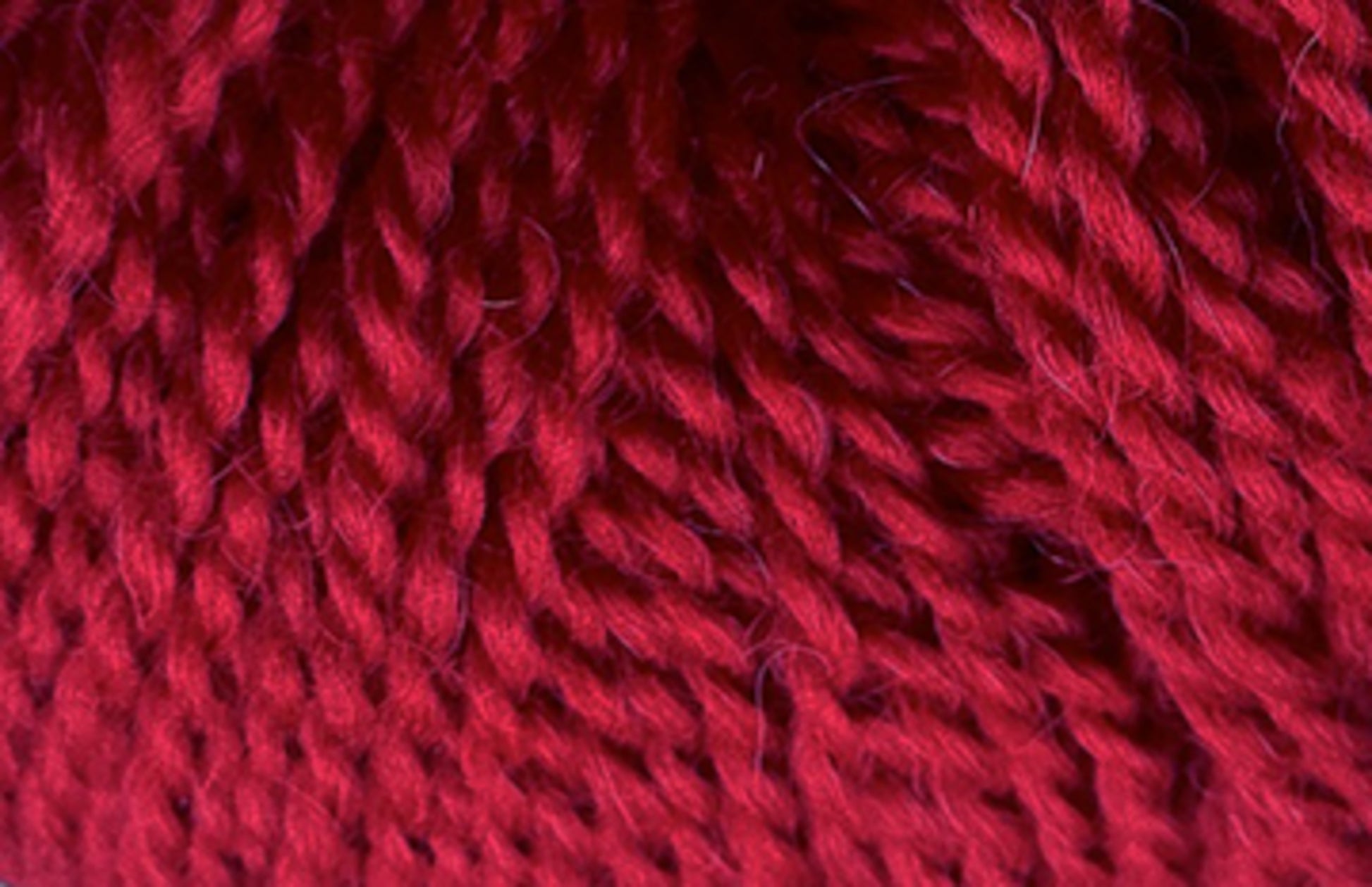 Close-up of dark red yarn, showcasing its thick, twisted fibers. The texture appears soft and slightly fuzzy, with a rich, deep hue. The image focuses on the intricate details of the Jo Sharp Alpaca Kid Lustre weave by Kingfisher Yarn & Fibre, highlighting the interplay of light and shadow on the material's surface.