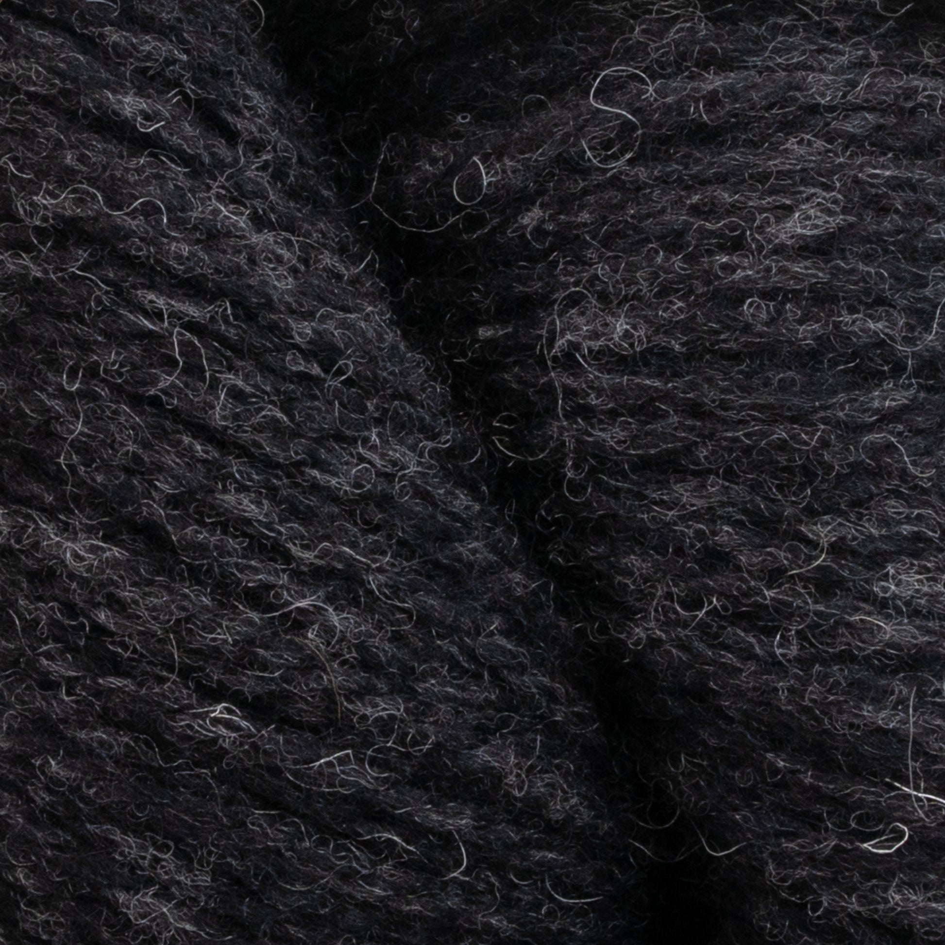 Close-up image of Patagonia Organic Merino by Juniper Moon Farm yarn with a textured, slightly fuzzy appearance. The dark gray-black fibers appear soft, and light gray strands interspersed throughout add a subtle pattern to the overall look. Made from GOTS certified organic Merino wool by Knitting Fever / Euro Yarns, it's perfect for your next eco-friendly project.